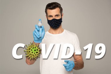 Lateks eldivenli ve güvenlik maskeli bir adam el dezenfektanını gri, covid-19 illüstrasyonunda izole etmiş. 