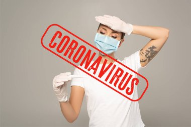Tıbbi maskeli, lateks eldivenli, termometre tutan ve alnına dokunan kadın gri, koronavirüs resimlerinde izole edilmiş.