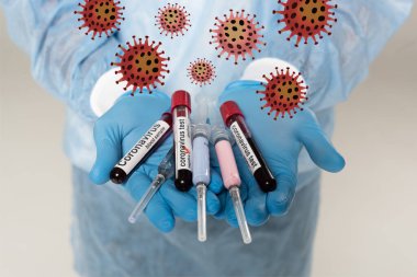 Doktorun elinde kan örnekleri, koronavirüs yazıları ve gri renkli şırıngalarla test tüpleri tuttuğunu gördüm.