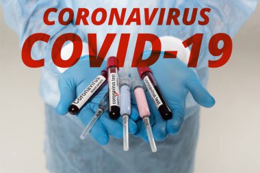 Cropped view of doctor holding test tubes with blood samples and coronavirus lettering and syringes isolated on grey, coronavirus covid-19 illustration clipart
