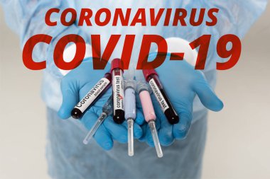 Cropped view of doctor holding test tubes with blood samples and coronavirus lettering and syringes isolated on grey, coronavirus covid-19 illustration clipart