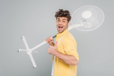 Ağzı açık, elinde elektrikli vantilatör olan heyecanlı bir adam kameraya bakıyor ve gri renkte izole bir tabela gibi görünüyor.