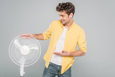 Gri renkte izole edilmiş elektrikli yelpazeye gülümseyen ve işaret eden adam