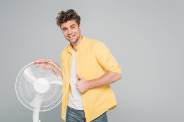Adam gülümsüyor, kameraya bakıyor ve gri renkte izole edilmiş elektrikli yelpaze gibi görünüyor.