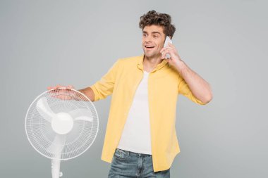 Gri renkte izole edilmiş elektrikli vantilatörün yanında gülümseyen ve konuşan bir adam.