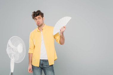 Elektrik ve el vantilatörlü bir adam griye bakıyor.