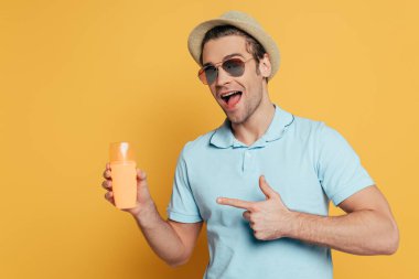 Excited man with open mouth pointing at bottle of sunscreen isolated on yellow  clipart