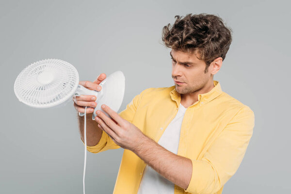 Concentrated man looking at desk fan isolated on grey