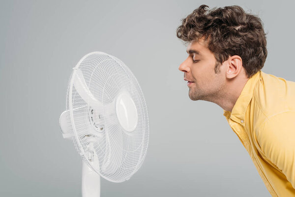 Man enjoying electric fan with closed eyes isolated on grey