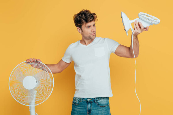 Concentrated and worried man looking at desk fan isolated on yellow