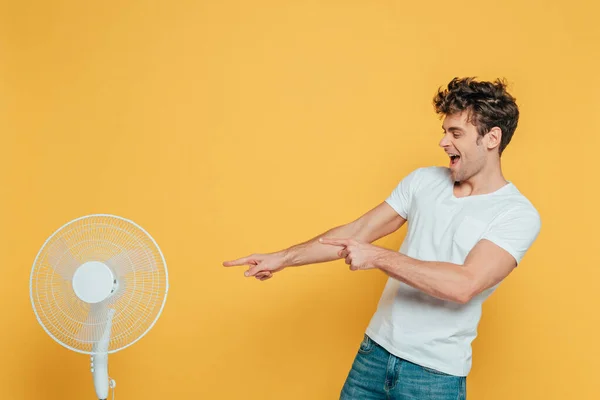 Homem Excitado Com Boca Aberta Apontando Para Ventilador Elétrico Isolado — Fotografia de Stock