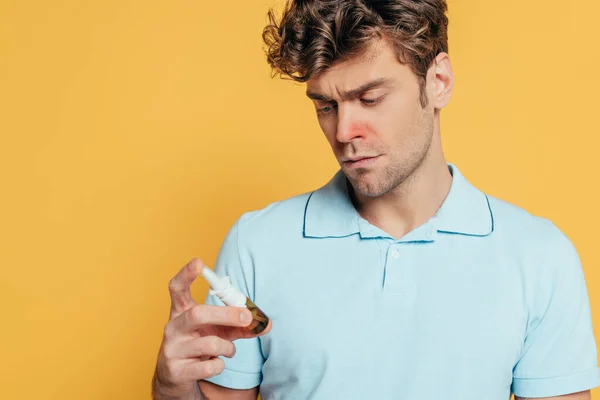 Hombre Enfermo Mirando Una Botella Gotas Nasales Aisladas Amarillo — Foto de Stock