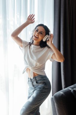 Evde kulaklıklarla dans edip müzik dinleyen genç bir kadın.