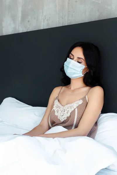 有魅力的睡意的女人 戴着医疗面罩 靠自我隔离坐在床上 — 图库照片