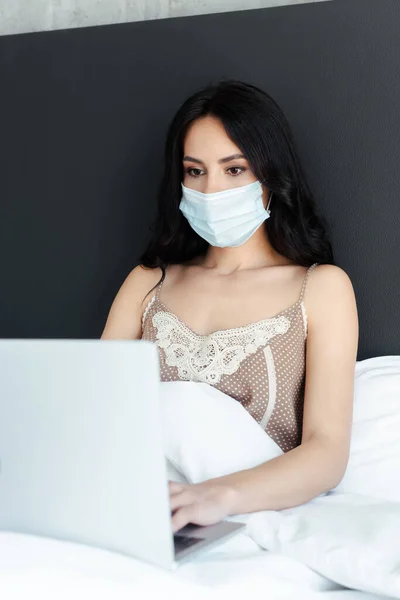 戴口罩的生病女孩在床上使用笔记本电脑进行自我隔离 — 图库照片