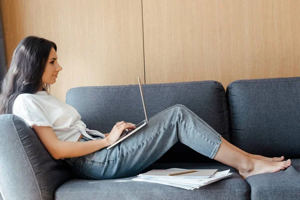 在笔记本电脑上工作的有魅力的女人 在自我隔离的时候把商务文件放在沙发上 — 图库照片