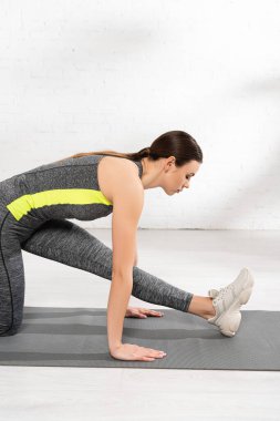 Spor merkezinde spor minderinin üzerinde esneyen esnek genç kadın profili 