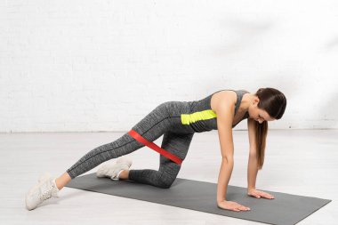 Sportif kadın spor paspasının üzerinde duruyor ve direniş bandıyla çalışıyor.