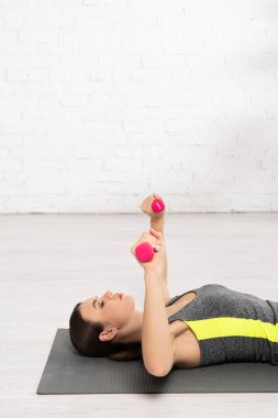 Dambıllarla egzersiz yapan ve spor minderinde uzanan genç sporcuların yan görünüşü