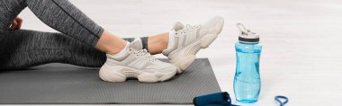 panoramic orientation of sportswoman sitting on fitness mat near sports bottle with water and skipping rope  clipart