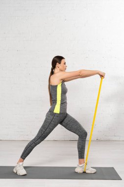 Beyaz tuğlalı duvarın yanında spor bantlı spor yapan bir kadının yan görüntüsü. 