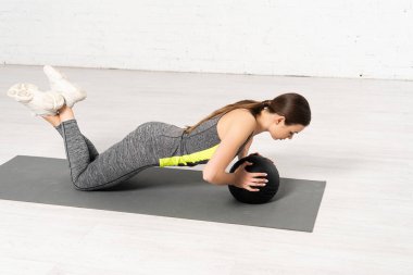 Spor giyim sektöründe çekici bir sporcu kadın spor minderinde siyah topla egzersiz yapıyor. 