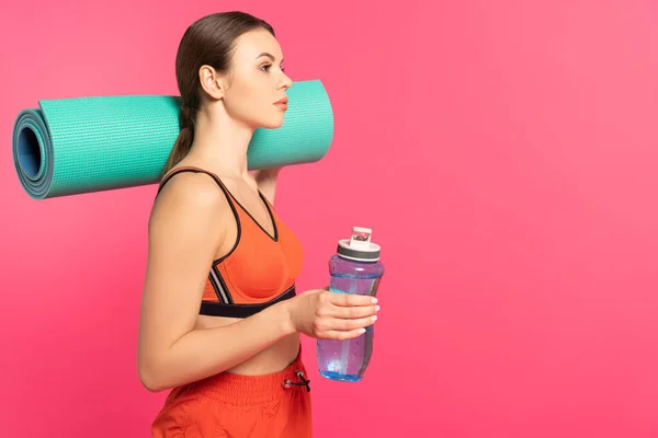 ピンクに隔離された水とフィットネスマットとスポーツボトルを保持する魅力的なスポーツ女性 — ストック写真