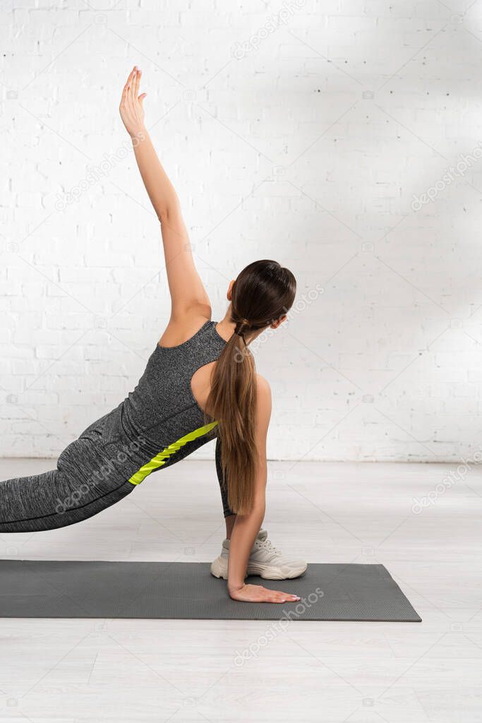 back view of sportive woman with outstretched hand exercising on fitness mat 