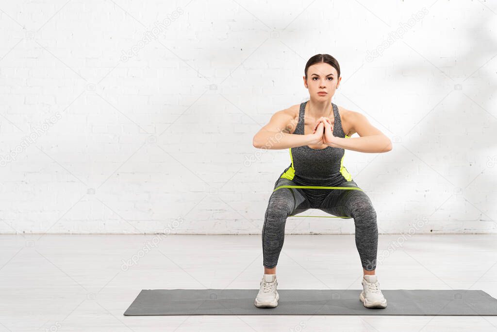 athletic girl with praying hands exercising with resistance band on fitness mat