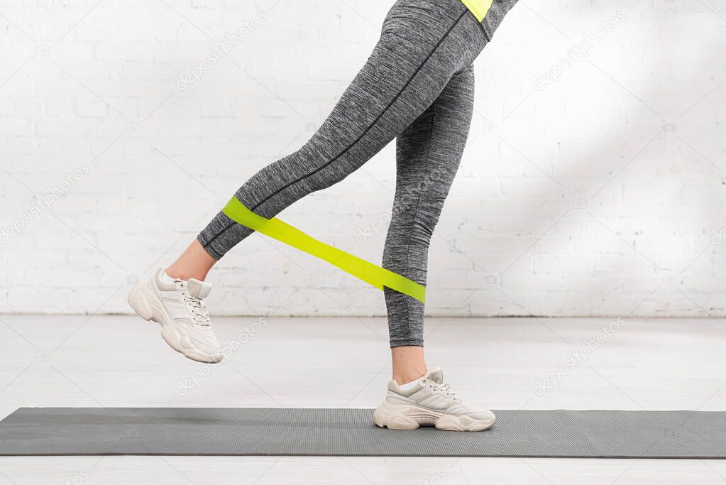 cropped view of woman exercising with resistance band on fitness mat