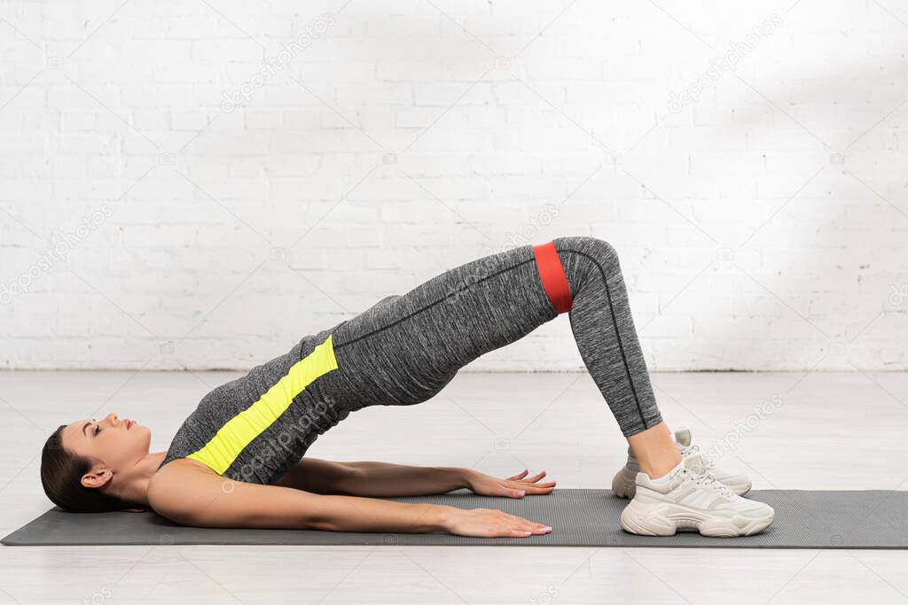 side view of sportive woman with working out with resistance band on fitness mat