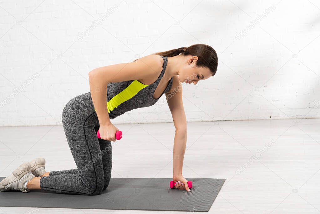 side view of athletic sportswoman exercising with dumbbells on fitness mat
