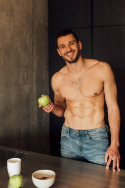 Mutfakta fincanın yanında elma tutan mutlu sakallı adam. 
