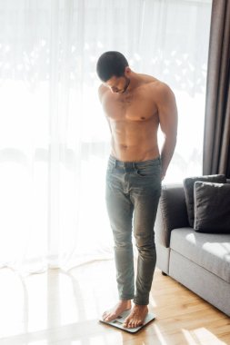 Oturma odasında terazinin üzerinde duran kaslı adam. 