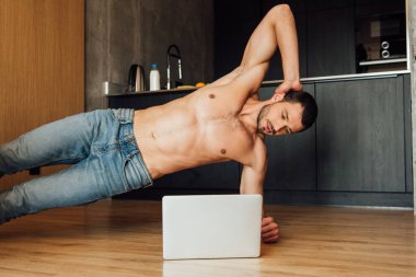 Üstsüz adam laptopta egzersiz yapıyor ve çevrimiçi eğitim izliyor. 