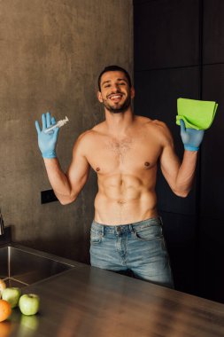 Neşeli ve kaslı bir adam elinde antiseptikle bez ve şişe tutuyor. 
