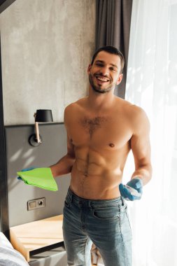 Lastik eldivenli neşeli ve kaslı bir adam elinde antibakteriyel sıvıyla bez ve şişe tutuyor.