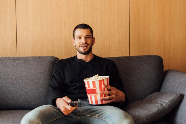 Šťastný Vousatý Muž Drží Dálkové Ovládání Popcorn Kbelík — Stock fotografie