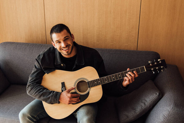 happy bearded man playing acoustic guitar in living room 