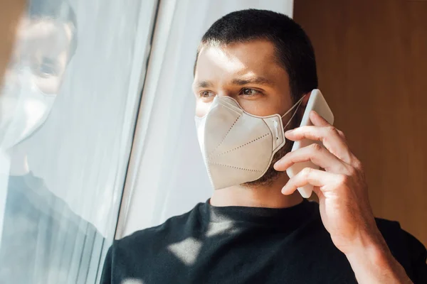 Hombre Máscara Médica Hablando Teléfono Inteligente Cerca Ventana —  Fotos de Stock