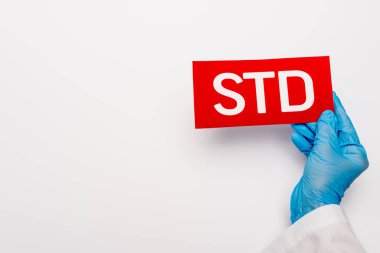cropped view of doctor in blue latex glove holding paper with std lettering on white  clipart