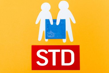 top view of paper people near blue condom and std lettering isolated on orange clipart