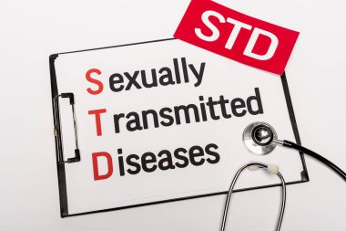 top view of clipboard with sexually transmitted diseases near paper with std lettering and stethoscope isolated on white clipart