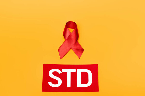 top view of red ribbon as hiv awareness near std lettering isolated on orange 