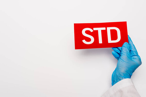 cropped view of doctor in blue latex glove holding paper with std lettering on white 