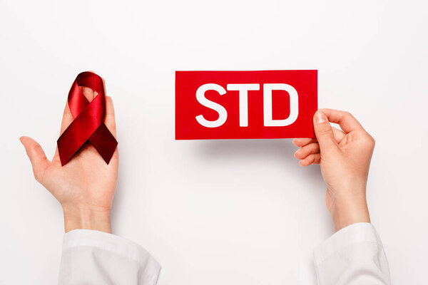 cropped view of doctor holding paper with std lettering and red ribbon on white 