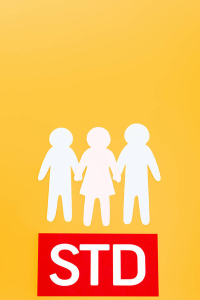 top view of three paper people near red paper with std lettering isolated on orange