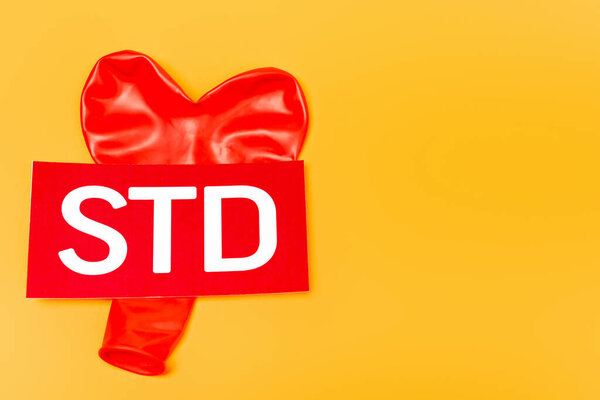 top view of heart-shaped balloon near std lettering isolated on orange 