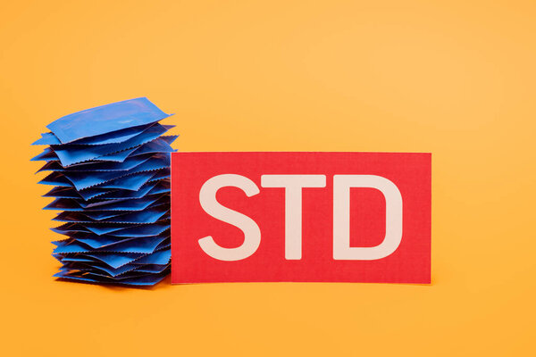 stack of condoms near paper with std lettering isolated on orange 