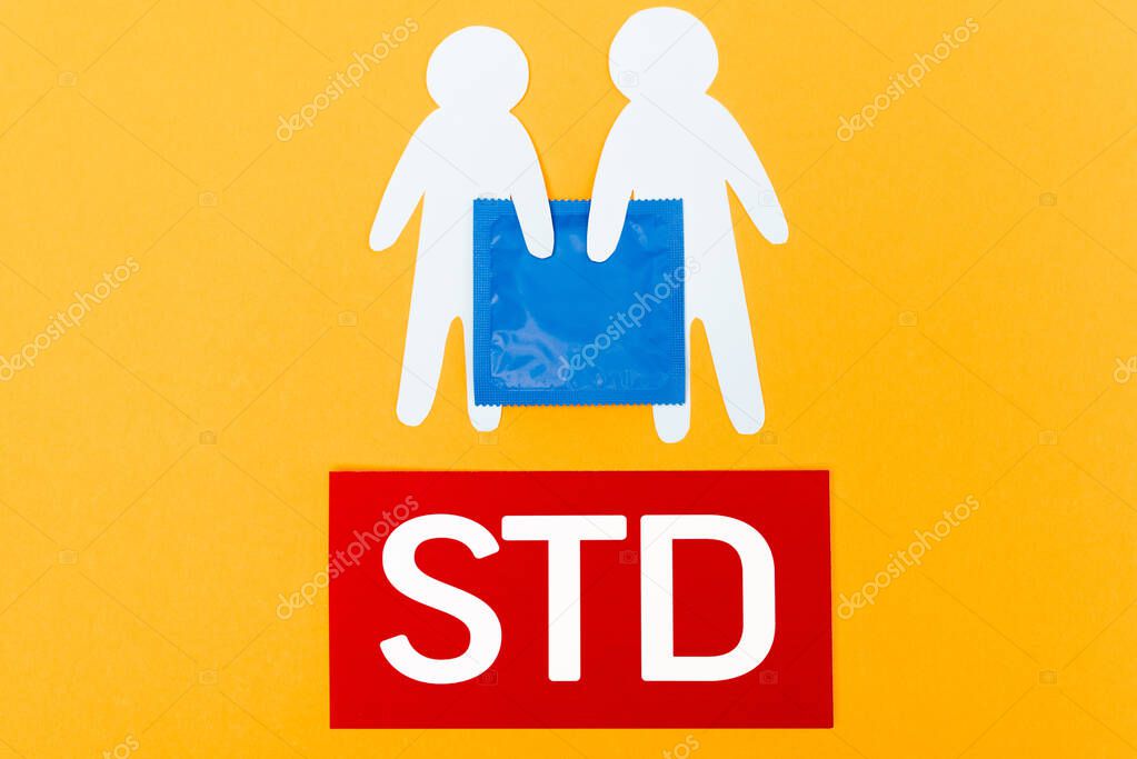top view of paper people near blue condom and std lettering isolated on orange